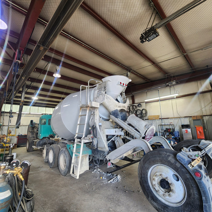 "Concrete mixer truck in a repair shop, receiving maintenance on its drum and other components to ensure optimal performance for heavy-duty construction tasks."